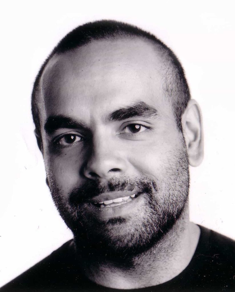 Bryan Andy's headshot in black and white. He is looking at smiling directly to the camera, has short shaven hair, and stubbled beard and mustache.